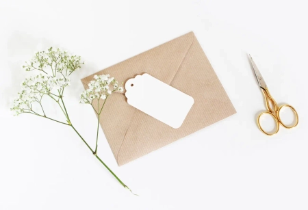 Papeterie mit Umschlag, Anhänger, Blumen und Schere als stimmungsvolles Motiv für Einladungskarten